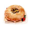 Ring-shaped muffaletta sandwich tray with deli meats, cheese, central olive mix, and cherry tomatoes garnish.